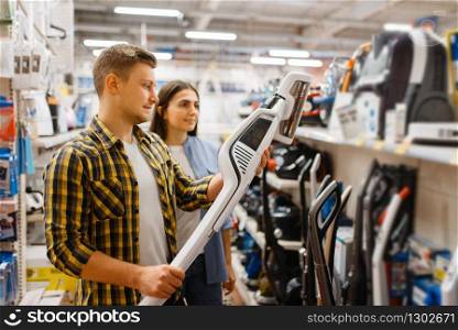Young couple choosing vacuum cleaner in electronics store. Man and woman buying home electrical appliances in market. Couple choosing vacuum cleaner, electronics store
