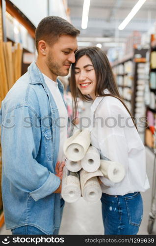Young couple choosing wallcovering in hardware store. Male and female customers look at the goods in diy shop. Couple choosing wallcovering in hardware store