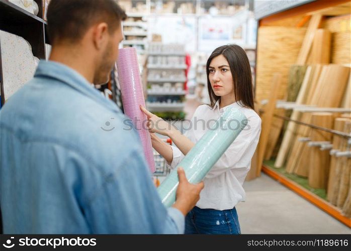 Young couple choosing wallpapers color in hardware store. Male and female customers look at the goods in diy shop