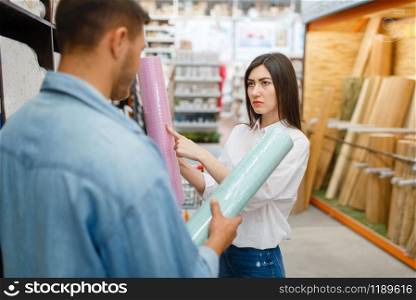 Young couple choosing wallpapers color in hardware store. Male and female customers look at the goods in diy shop