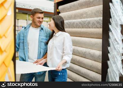 Young couple choosing wallpapers in hardware store. Male and female customers look at the goods in diy shop