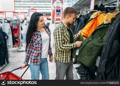 Young couple choosing warm clothes in supermarket. Male and female customers on family shopping. Man and woman purchasing goods for the house. Young couple choosing warm clothes in supermarket