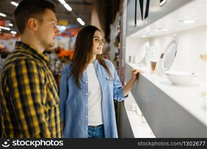 Young couple choosing wineglasses in houseware store. Man and woman buying home goods in market, family in kitchenware supply shop. Couple choosing wine glasses in houseware store