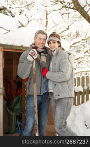 Young Couple Clearing Snow From Path To Wooden Store