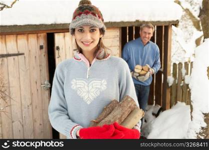 Young Couple Collecting Logs From Wooden Store In Snow