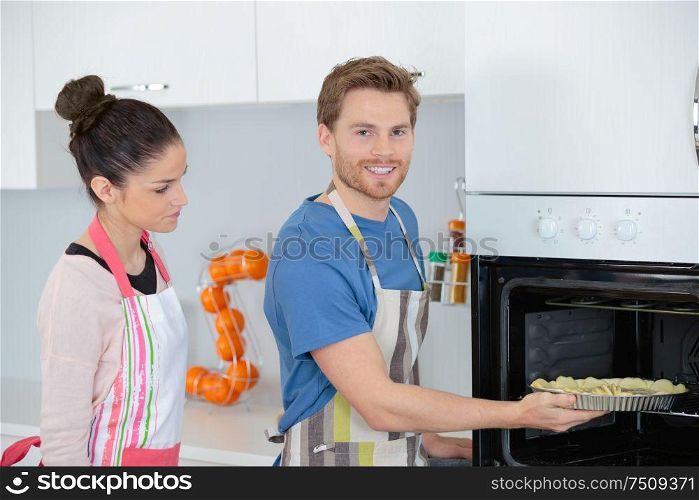 young couple cooking at home stood by oven