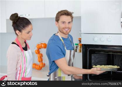young couple cooking at home stood by oven