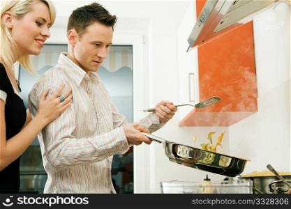 Young couple cooking in their kitchen at home. Selective focus on his face and cooking gear