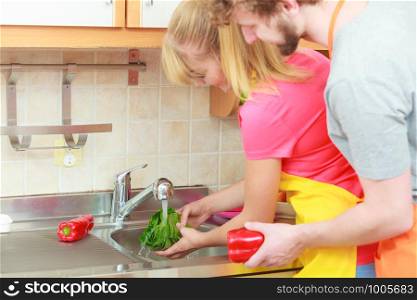 Young couple cooking together, washing fresh vegetables red pepper green lettuce in kitchen under water stream, preparation salad vegetarian meal