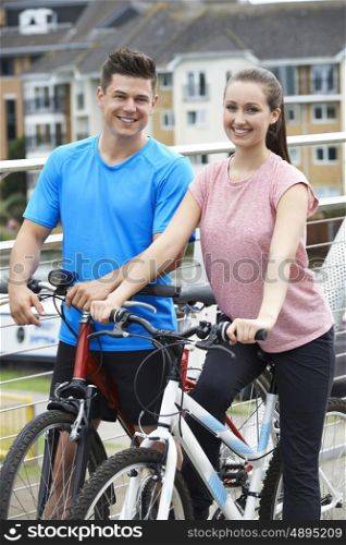 Young Couple Cycling Next To River In Urban Setting