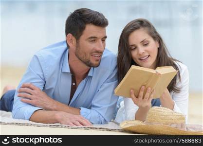young couple dating on the beach reading a book