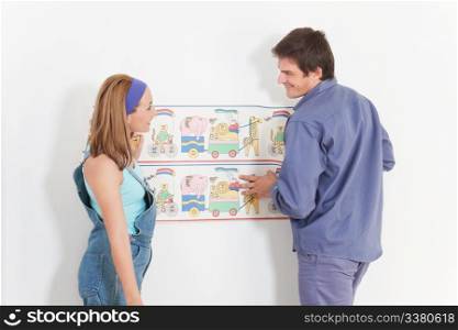 Young couple decorating a baby room with wallpaper