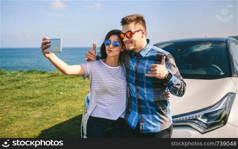 Young couple doing a selfie leaning on the car near the coast. Young couple doing a selfie on the car