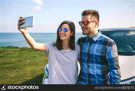 Young couple doing a selfie leaning on the car near the coast. Young couple doing a selfie on the car