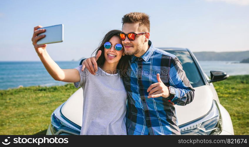 Young couple doing a selfie leaning on the car near the coast. Young couple doing a selfie on the car