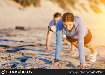 Young couple doing push ups on ocean beach. Young couple of man and woman doing push ups on ocean beach