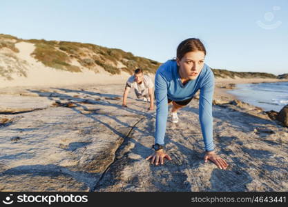 Young couple doing push ups on ocean beach. Young couple of man and woman doing push ups on ocean beach