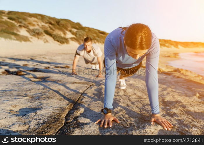 Young couple doing push ups on ocean beach. Young couple of man and woman doing push ups on ocean beach