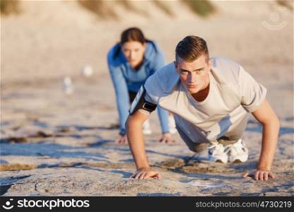 Young couple doing push ups on ocean beach. Young couple of man and woman doing push ups on ocean beach