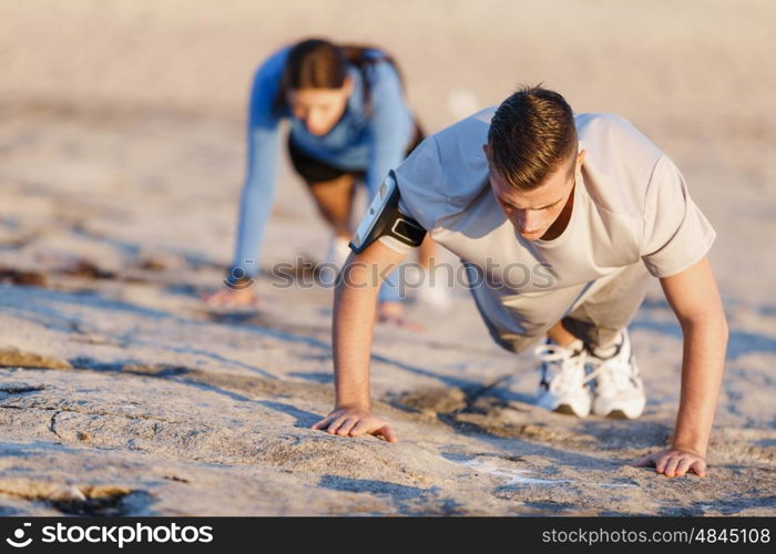 Young couple doing push ups on ocean beach. Young couple of man and woman doing push ups on ocean beach