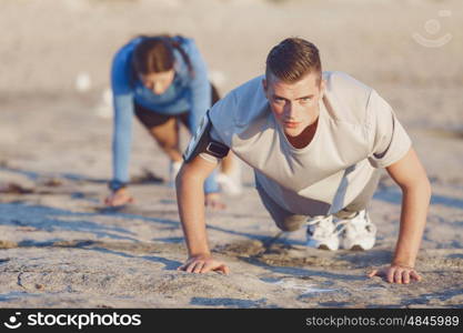 Young couple doing push ups on ocean beach. Young couple of man and woman doing push ups on ocean beach