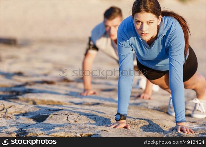 Young couple doing push ups on ocean beach. Young couple of man and woman doing push ups on ocean beach