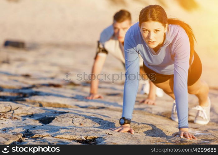 Young couple doing push ups on ocean beach. Young couple of man and woman doing push ups on ocean beach