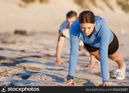 Young couple doing push ups on ocean beach. Young couple of man and woman doing push ups on ocean beach