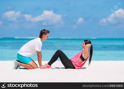 Young couple doing sport exercises on the beach. Young couple do abdominal crunches on white beach during vacation