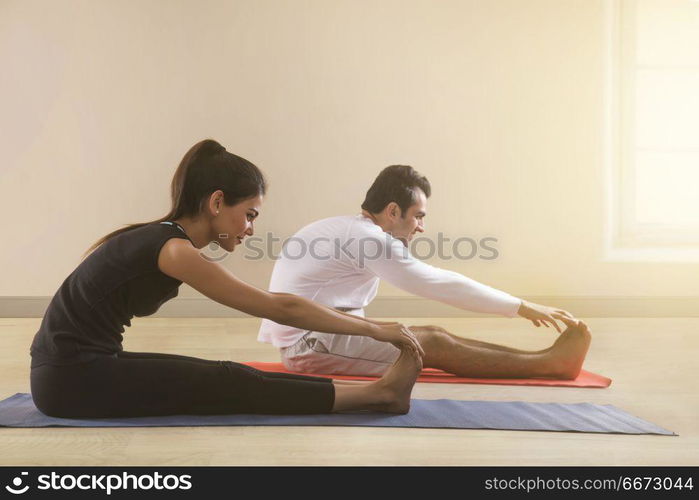 Young couple doing stretching exercise on yoga mat