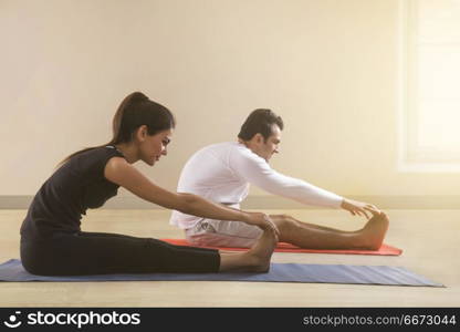 Young couple doing stretching exercise on yoga mat