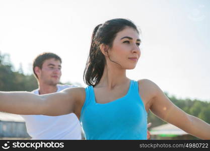 Young couple doing stretching yoga exercises with sea on the background