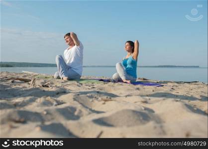 Young couple doing stretching yoga exercises with sea on the background