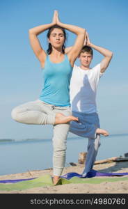 Young couple doing stretching yoga exercises with sea on the background