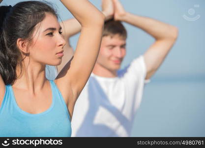 Young couple doing stretching yoga exercises with sea on the background