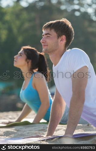 Young couple doing stretching yoga exercises with sea on the background