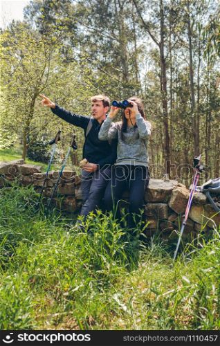 Young couple doing trekking looking at the landscape with binoculars
