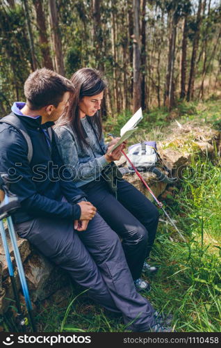 Young couple doing trekking sitting looking at a map outdoors. Couple doing trekking sitting looking at a map