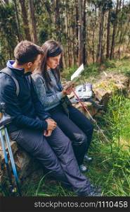 Young couple doing trekking sitting looking at a map outdoors. Couple doing trekking sitting looking at a map