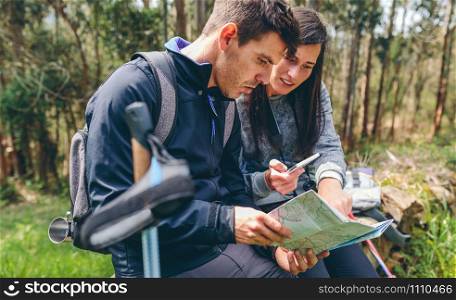 Young couple doing trekking sitting looking mobile and map outdoors. Couple doing trekking sitting looking mobile and map