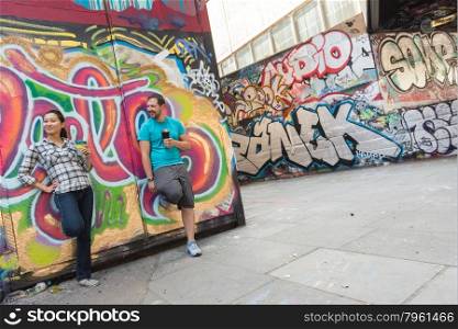 Young Couple Drinking Coffee and Chatting in Concrete Urban Skate park with Very Colorful and Vibrant Graffiti