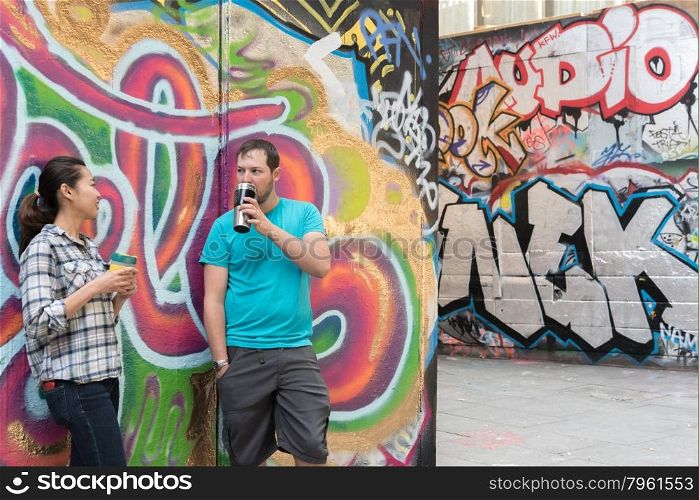 Young Couple Drinking Coffee and Chatting in Concrete Urban Skate park with Very Colorful and Vibrant Graffiti
