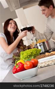 Young couple drinking red wine in kitchen, focus on bowl with vegetable
