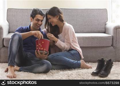 Young couple eating popcorn sitting on floor