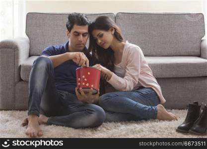 Young couple eating popcorn sitting on floor