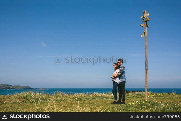 Young couple embraced by a direction sign on the coast. Couple embraced by a direction sign