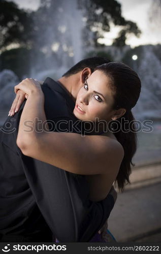 Young couple embracing by fountain in plaza, sunset