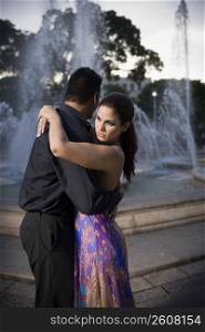 Young couple embracing by fountain in plaza, sunset