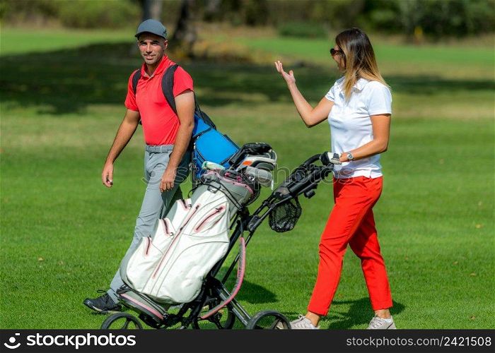 Young couple enjoying a game of golf, walking the fairway on a golf course on a beautiful sunny day