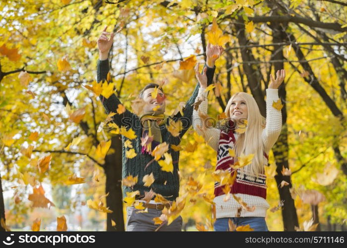 Young couple enjoying falling autumn leaves in park